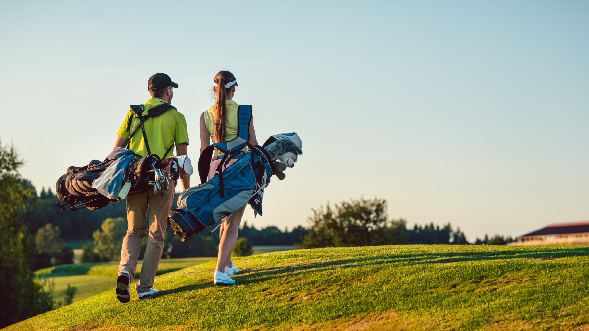 Un ccouple porte des tenues de golf et portent des sacs de club sur un terrain de golf en après-midi l'été