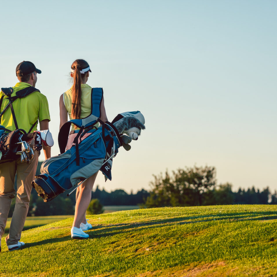 Un ccouple porte des tenues de golf et portent des sacs de club sur un terrain de golf en après-midi l'été