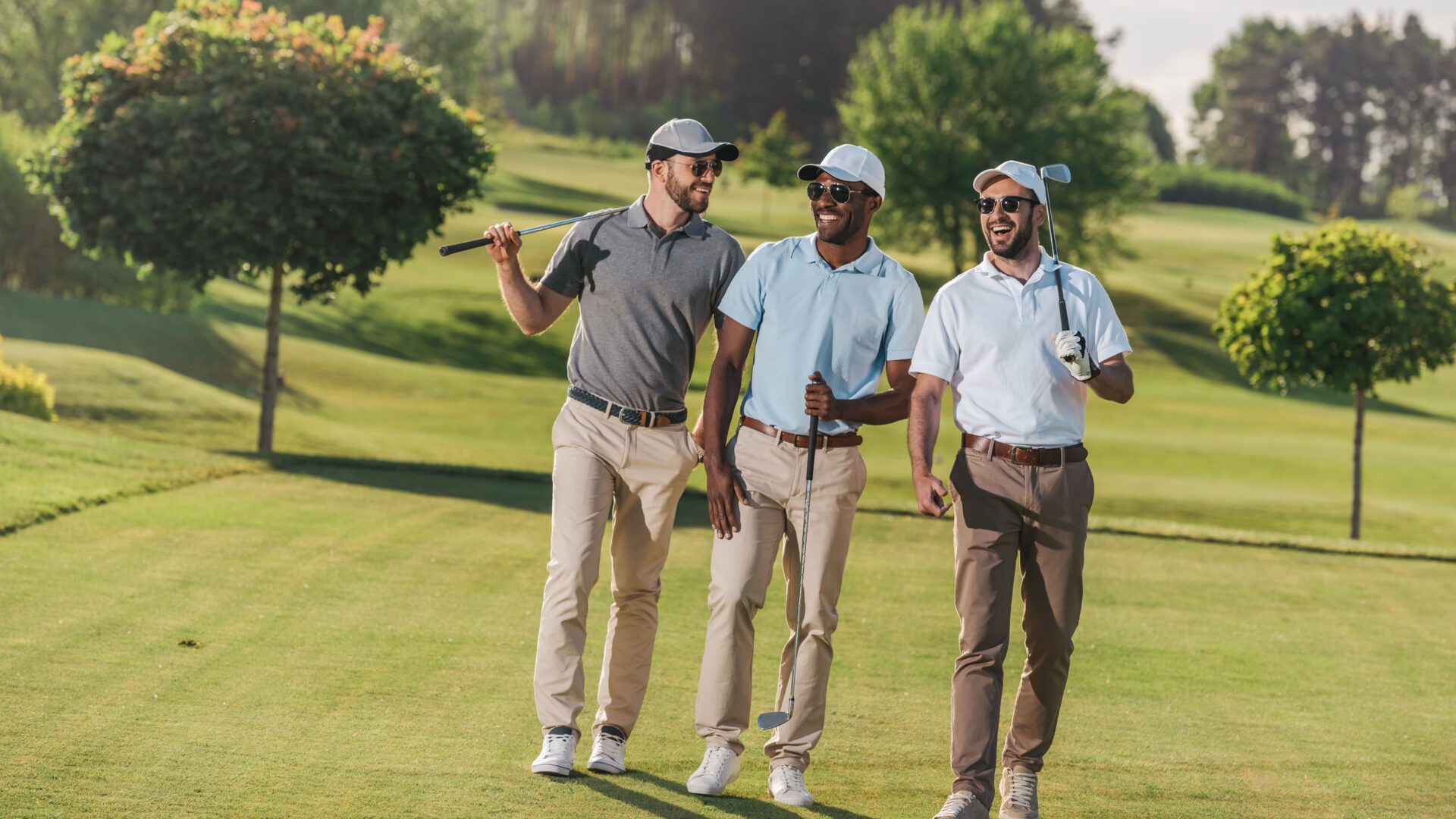 Hommes confiants portant des casquettes et des lunettes de soleil sur un terrain de golf, et tenant des clubs de golf