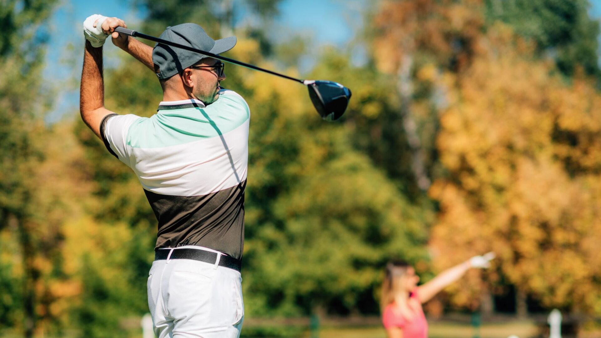 Couple de golfeurs jouant ensemble, un homme tire sur un fond boisé avec du bokeh