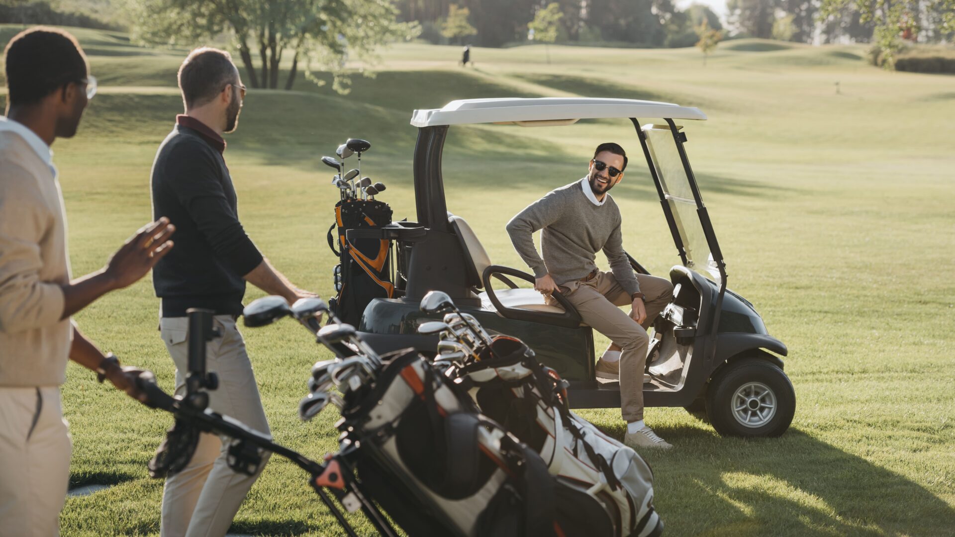 Amis jouant au golf sur un terrain, un est dans un caddie, les autres portent des sacs de clubs de golf.